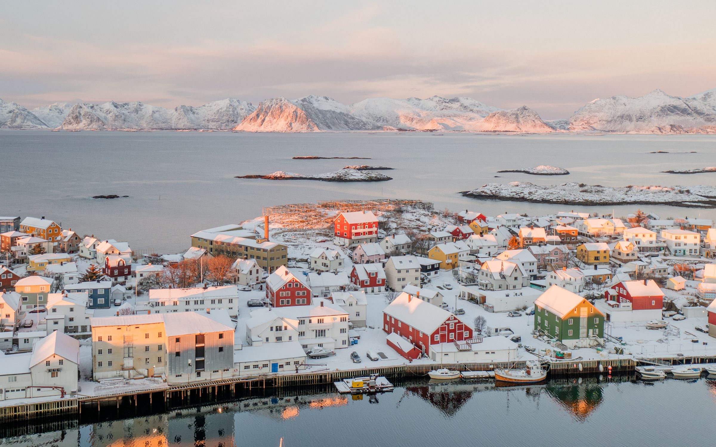 A snow-covered fishing village with wooden houses along the harbour and fish-drying racks behind
